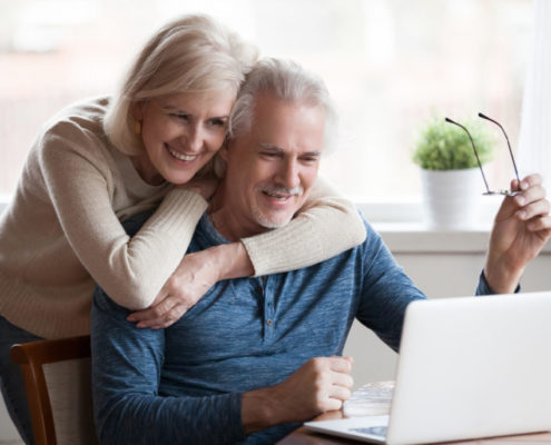 a man with Parkinson's at home on his laptop with his wife next to him