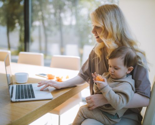 a young child learning from home on a laptop with a mother