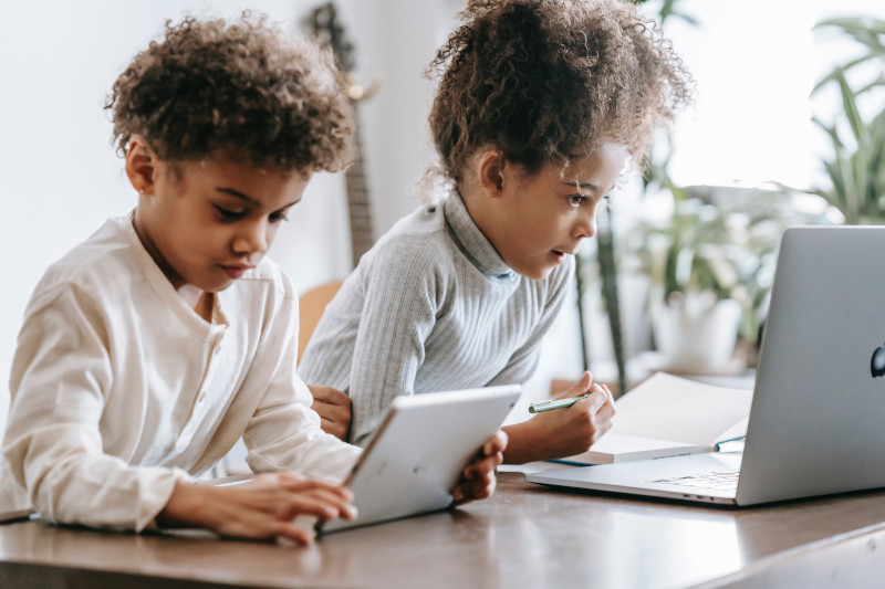 two children on laptops from home doing summer school