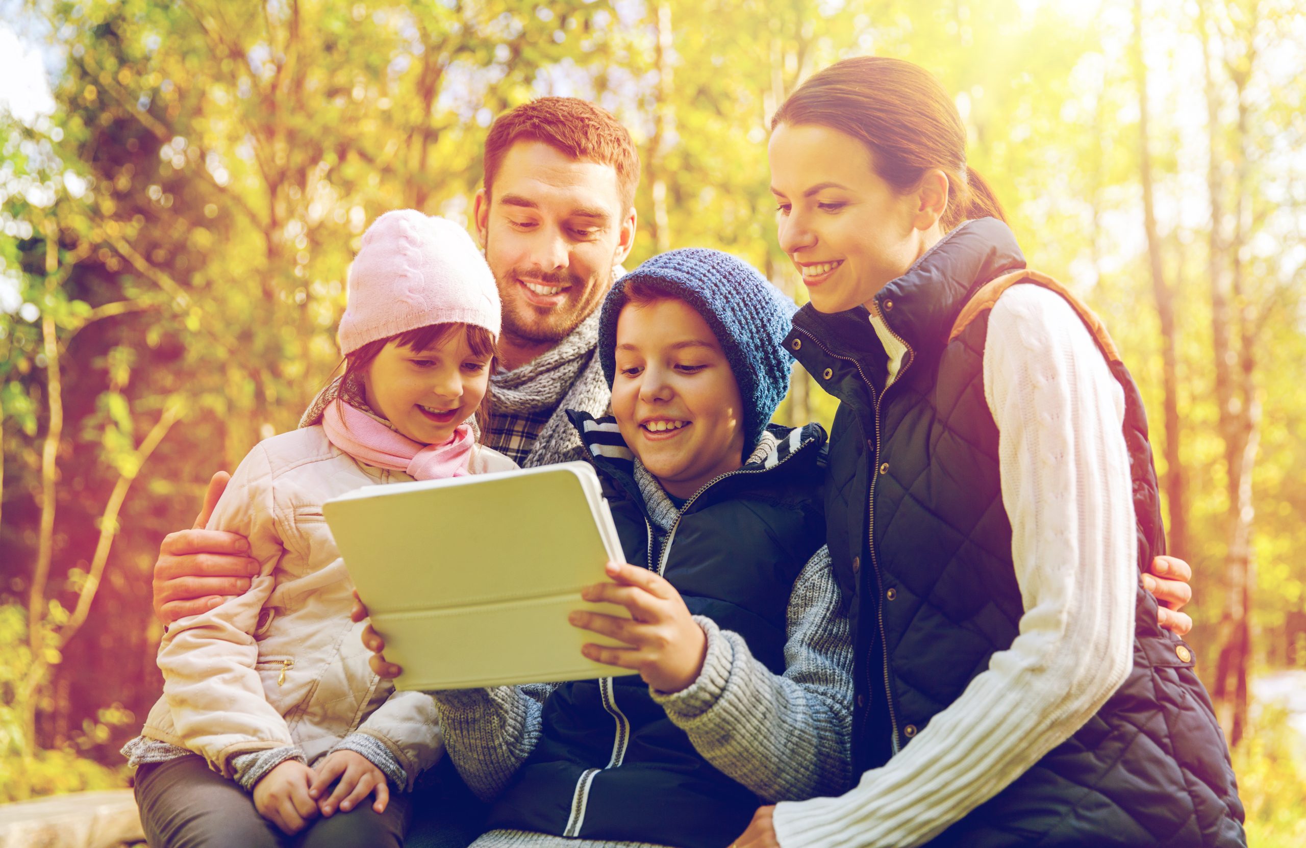 family in the woods smiling while looking at a tablet computer