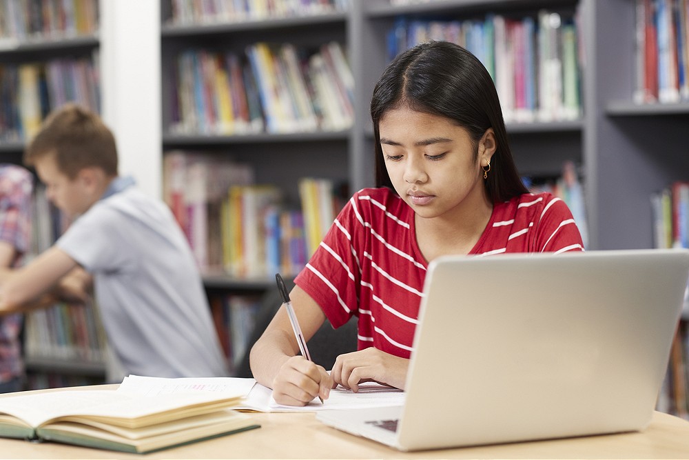 Female High School Student Working At Laptop In Library representing Benefit from Speech and Language Therapy